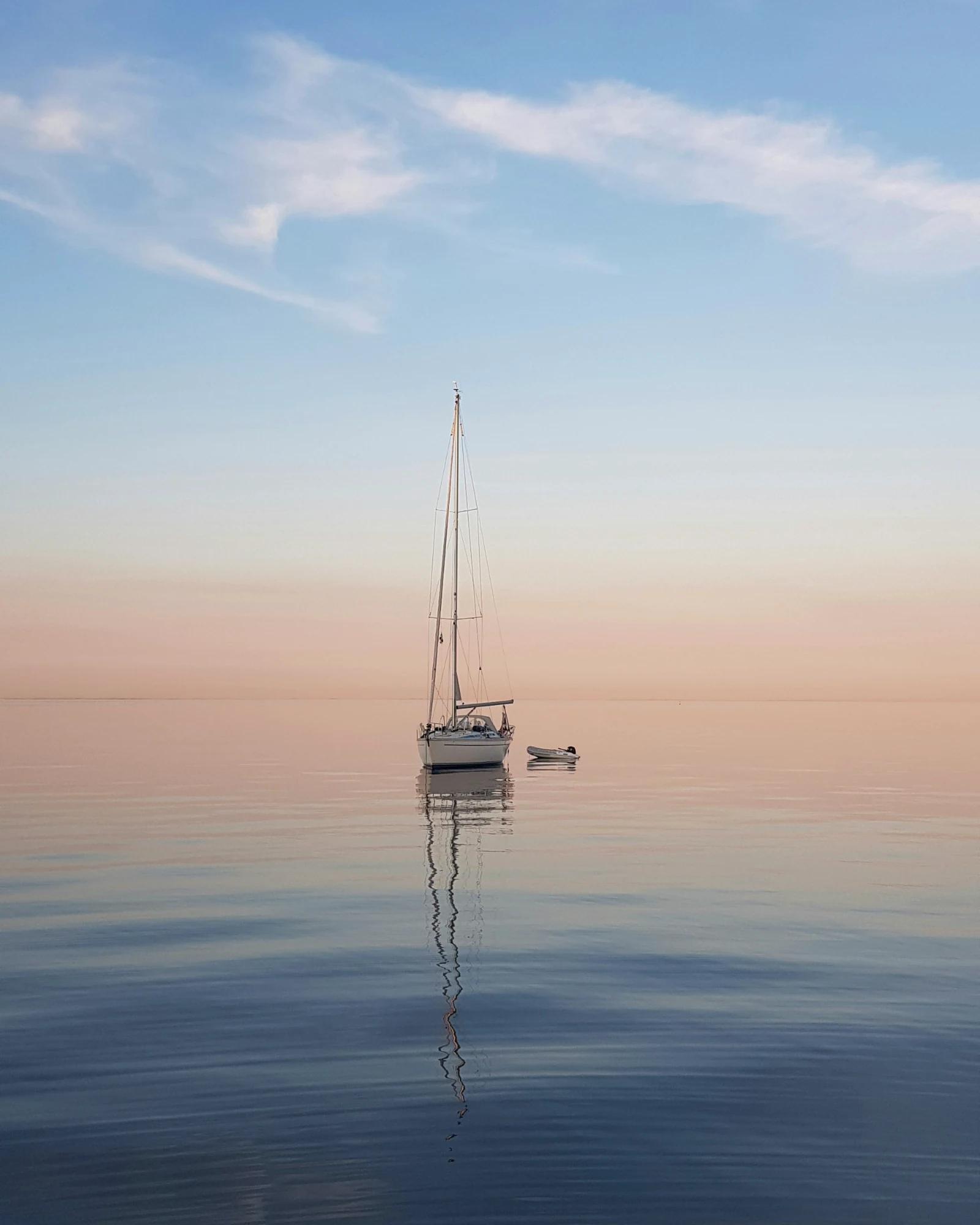 A single sailboat at anchor on still water at sunset